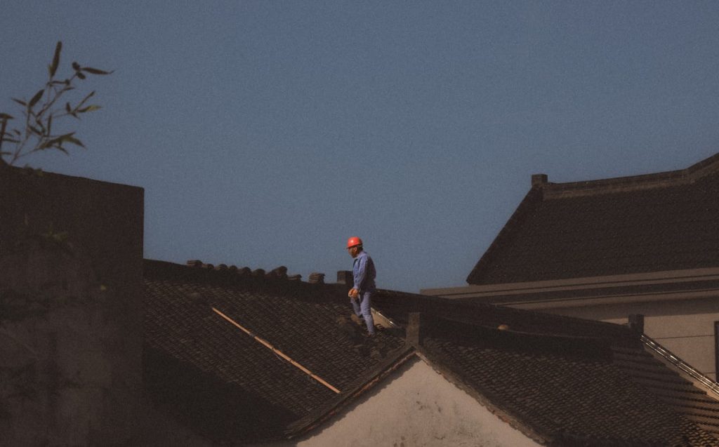 A construction worker with a red helmet standing on a roof on a clear day.